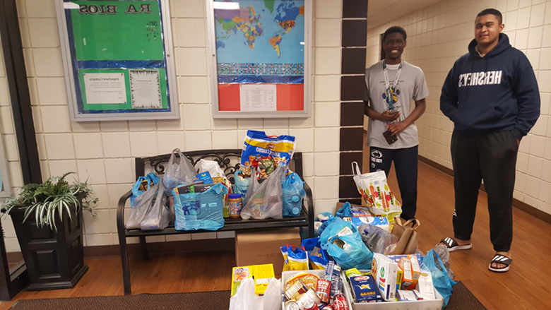 Two students stand by donated food and paper products